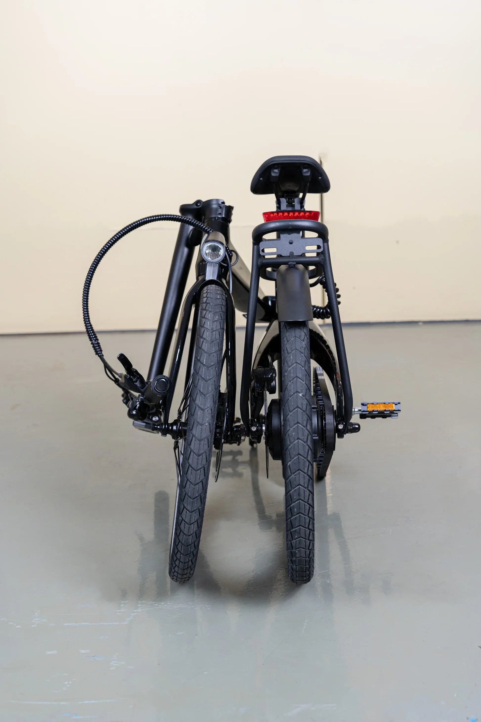 Folded black Electric bike with rear red reflector and front headlight on gray floor