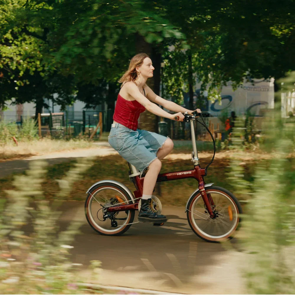 Woman riding a red Heybike Helio folding electric bike on a park path with trees