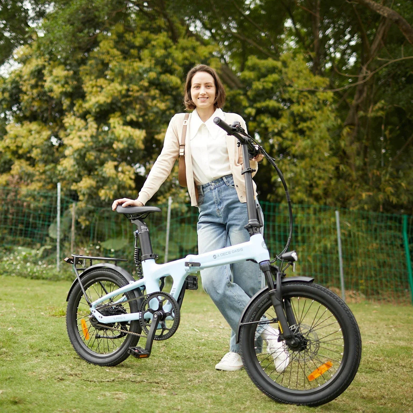 Woman standing outdoors with a light blue ADO Air Pro electric folding bike on grass