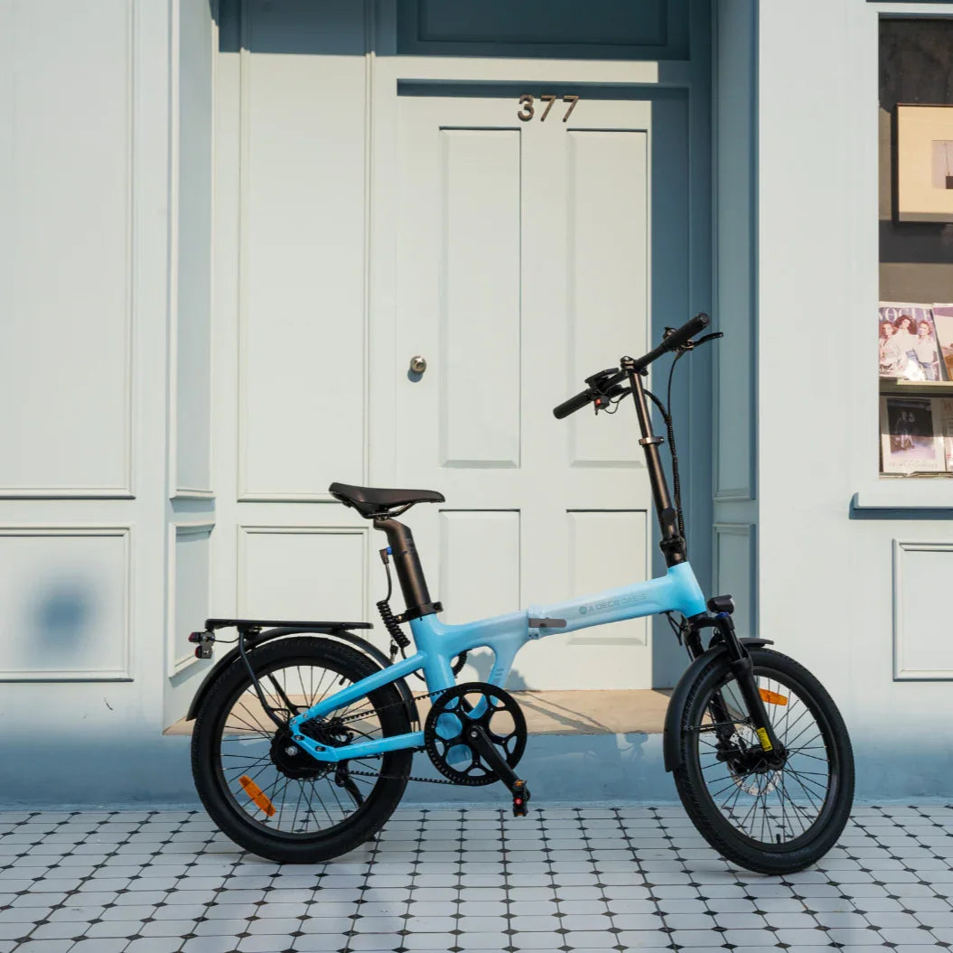 Blue foldable electric bike parked on patterned tile floor in front of pale blue door numbered 377