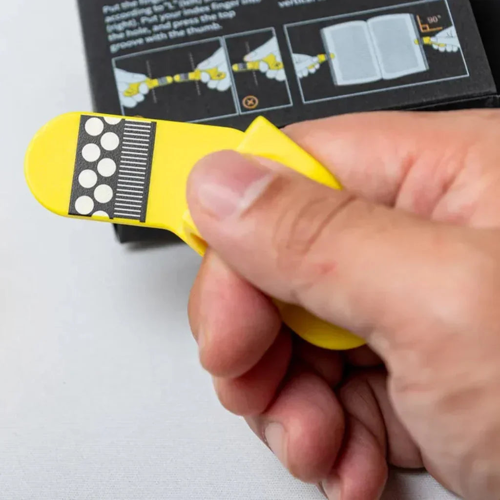 Hand holding yellow guitar finger cot pick with black and white grip dots, packaging with playing instructions in background