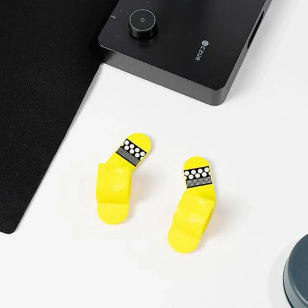 Two yellow CZUR finger cots with black and white dotted patterns on a white table near a black electronic device