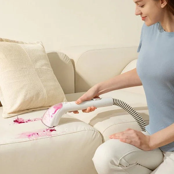 Woman using a white handheld spot cleaner to remove pink stains from a light beige sofa cushion