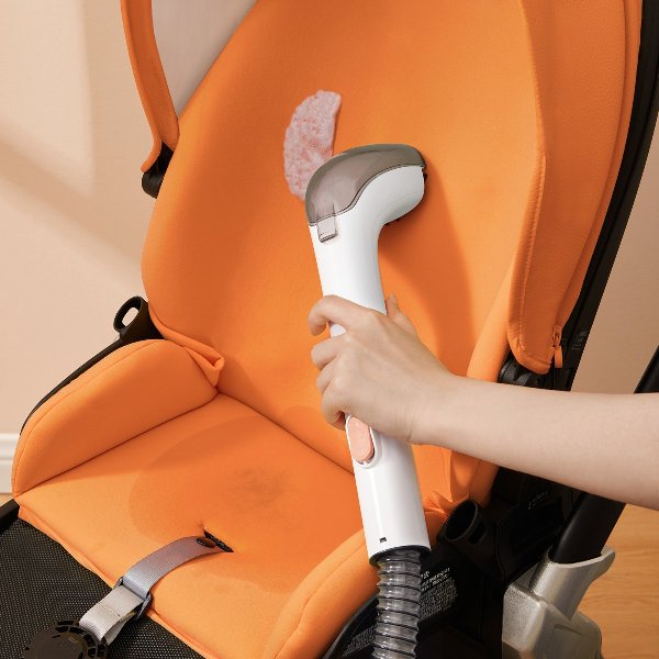 Hand using white and gray handheld carpet cleaner on stained orange stroller seat fabric