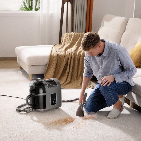 Person using a black Uwant B200 steam spot cleaner on a beige carpet stain in a bright living room with a white sofa and brown blanket